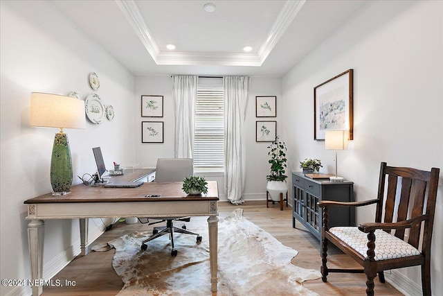 office area featuring light wood-style flooring, baseboards, a raised ceiling, and crown molding