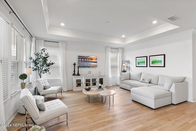 living area with light wood finished floors, a raised ceiling, visible vents, and crown molding