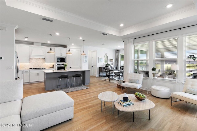 living area with light wood-style floors, a raised ceiling, visible vents, and crown molding