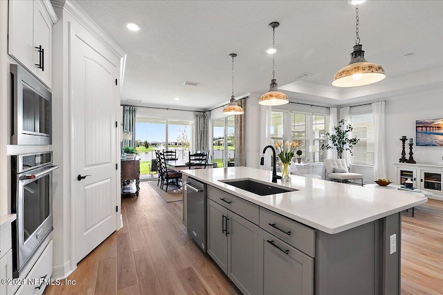 kitchen featuring a kitchen island with sink, gray cabinetry, stainless steel appliances, a sink, and light countertops