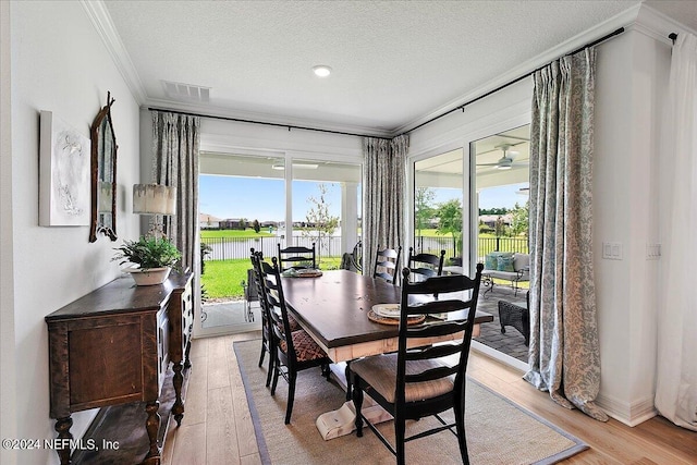 dining room featuring a textured ceiling, light wood finished floors, visible vents, and crown molding