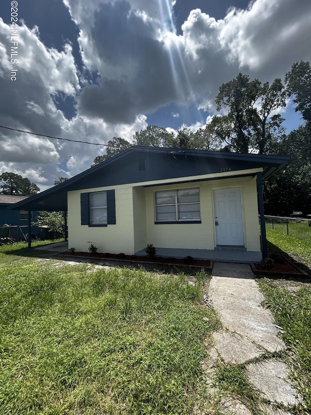 single story home featuring a carport, concrete block siding, and a front lawn