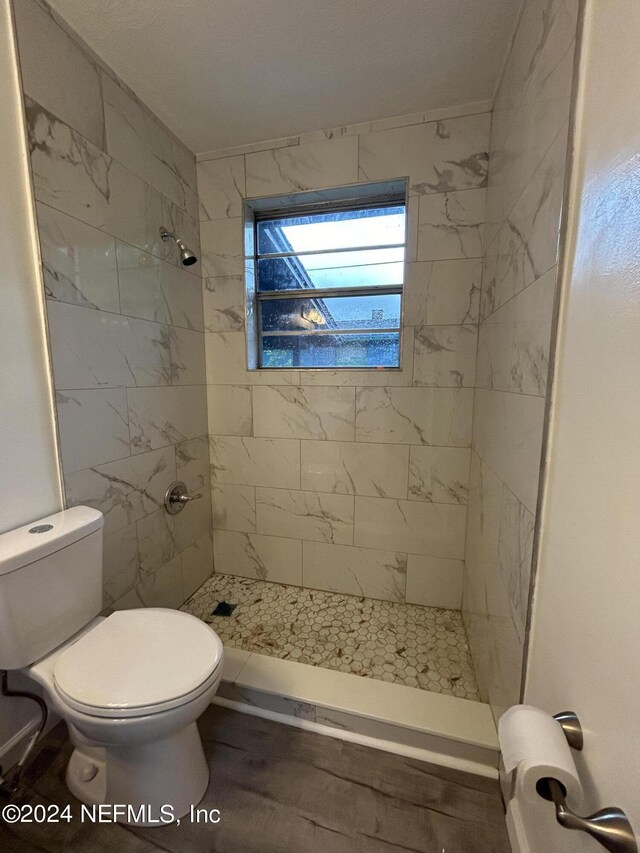 bathroom with toilet, wood-type flooring, and tiled shower