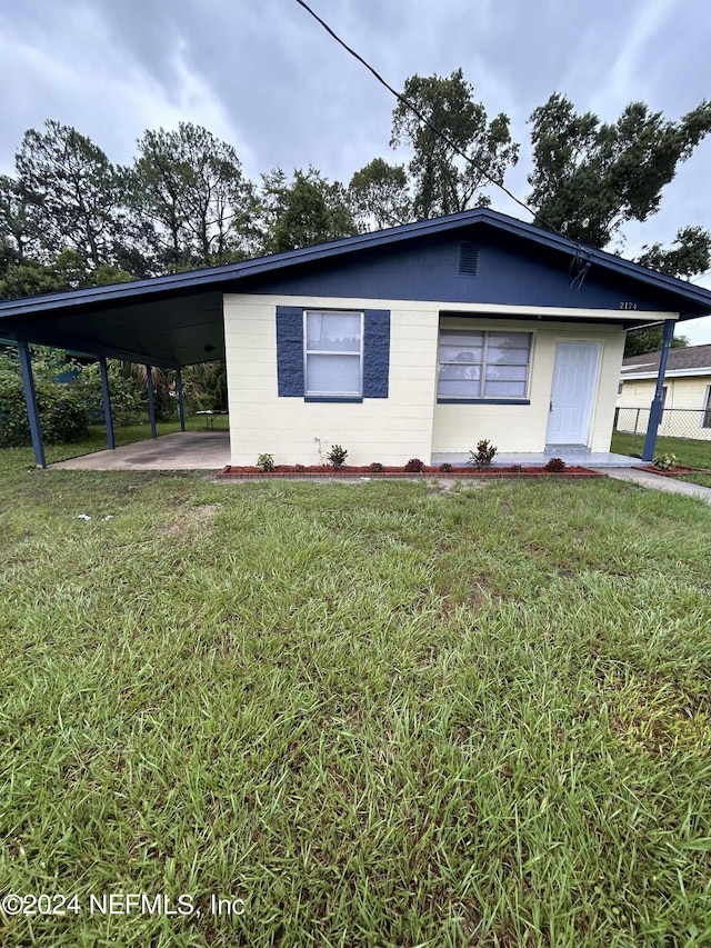 view of side of property with an attached carport, concrete block siding, a yard, and fence