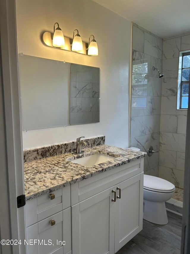 bathroom with tiled shower, wood-type flooring, toilet, and vanity