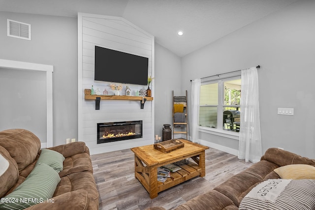 living area with a large fireplace, visible vents, vaulted ceiling, and wood finished floors