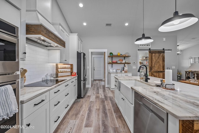 kitchen with a barn door, custom range hood, a kitchen island with sink, stainless steel appliances, and open shelves