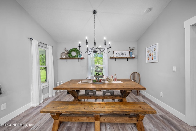 dining space with a notable chandelier, wood finished floors, lofted ceiling, and baseboards