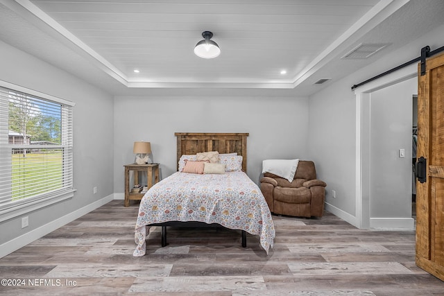 bedroom with a barn door, visible vents, a raised ceiling, and baseboards