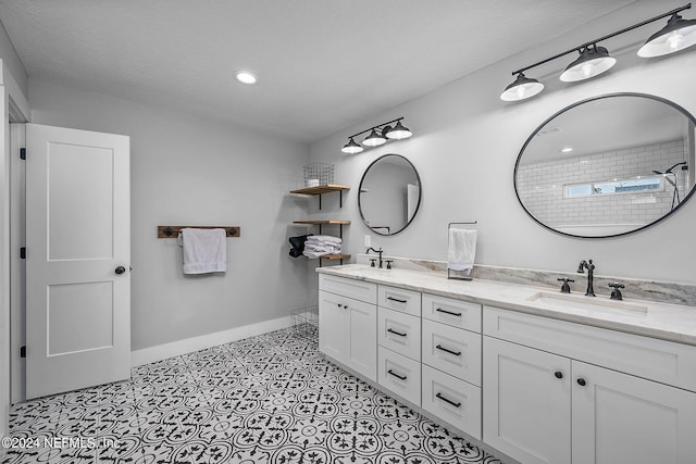 full bath with a sink, a textured ceiling, baseboards, and double vanity