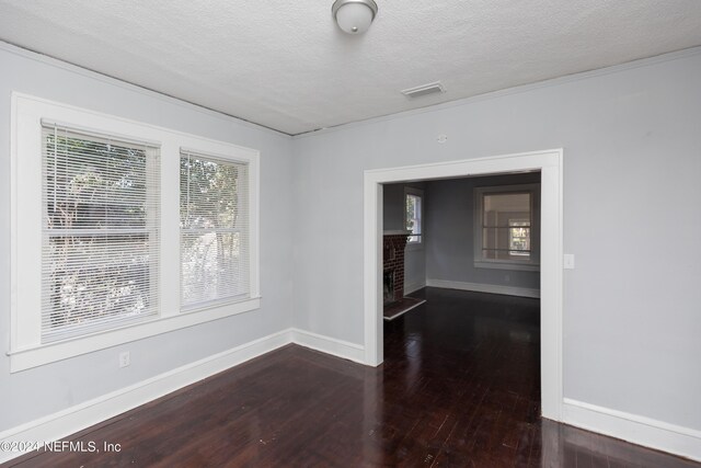 unfurnished room with a textured ceiling, a healthy amount of sunlight, dark hardwood / wood-style floors, and a brick fireplace