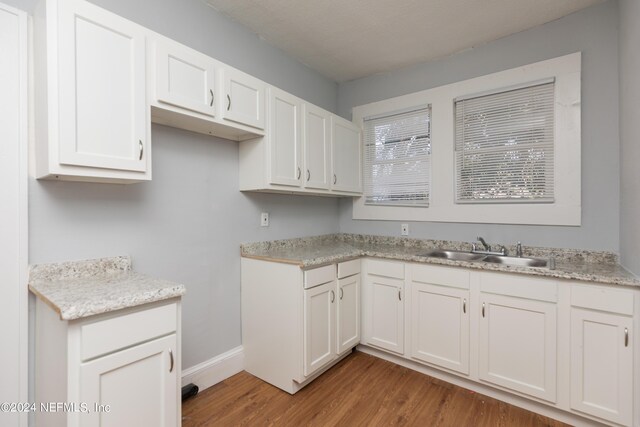 kitchen featuring light wood-type flooring, sink, light stone counters, and white cabinets