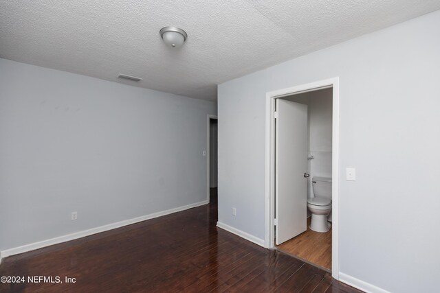 unfurnished bedroom featuring a textured ceiling, ensuite bath, and dark hardwood / wood-style flooring