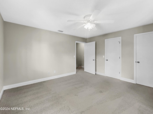 unfurnished bedroom with ceiling fan, light colored carpet, and multiple closets