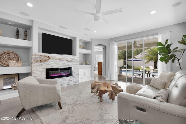 tiled living room with a stone fireplace, ceiling fan, and built in shelves