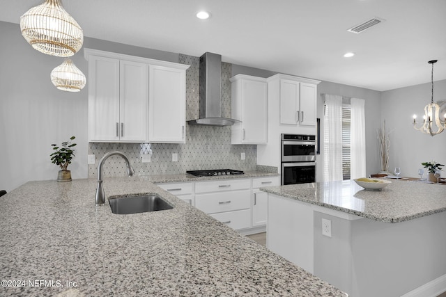 kitchen featuring sink, double oven, hanging light fixtures, white cabinets, and wall chimney exhaust hood