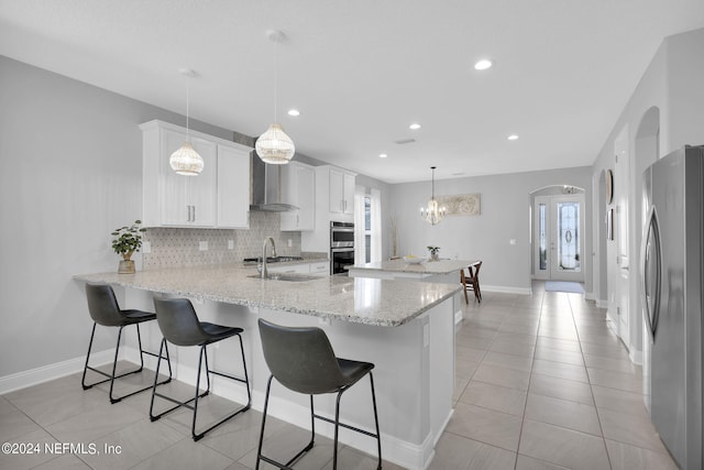 kitchen with wall chimney exhaust hood, sink, hanging light fixtures, appliances with stainless steel finishes, and white cabinets