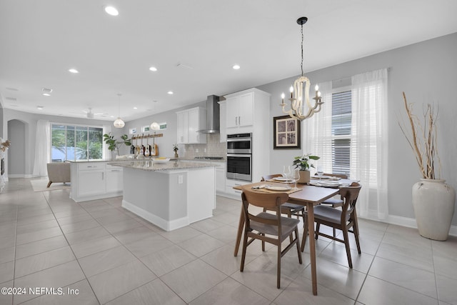 kitchen with wall chimney exhaust hood, cooktop, white cabinetry, a center island, and pendant lighting