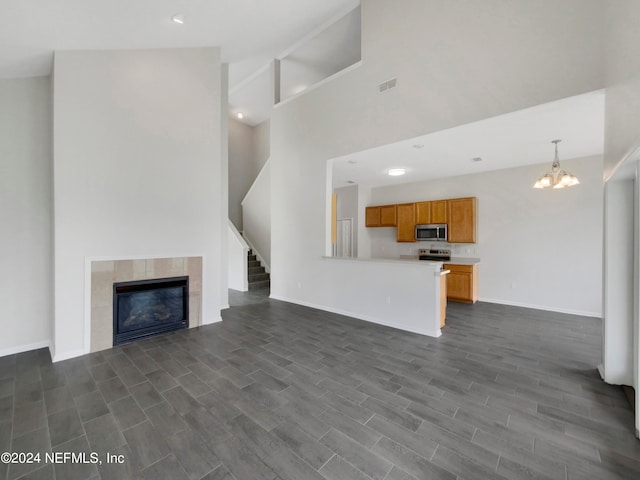 unfurnished living room featuring dark wood-type flooring, a towering ceiling, a tiled fireplace, and a notable chandelier