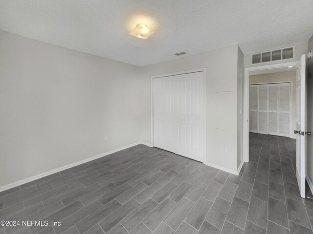 unfurnished bedroom with dark wood-type flooring, a textured ceiling, and a closet