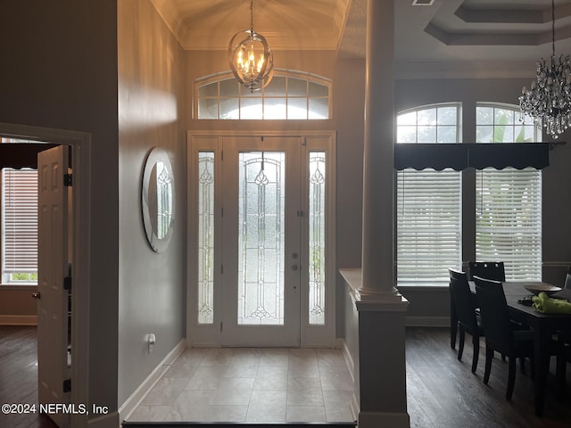 entryway with hardwood / wood-style floors, a tray ceiling, a chandelier, and ornate columns