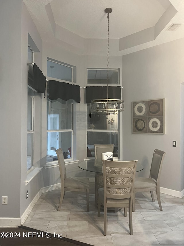 dining area featuring light tile patterned floors, an inviting chandelier, and a raised ceiling