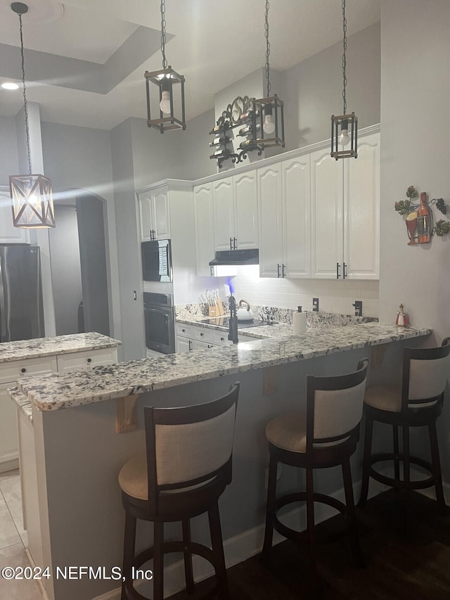 kitchen with appliances with stainless steel finishes, a kitchen bar, decorative backsplash, light stone counters, and white cabinets