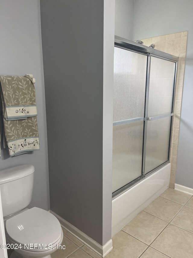 bathroom with combined bath / shower with glass door, toilet, and tile patterned floors