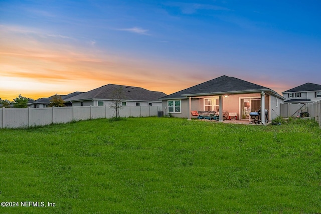 back house at dusk with a patio area and a yard