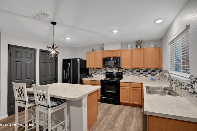 kitchen with light hardwood / wood-style flooring, black appliances, sink, a kitchen island, and decorative backsplash