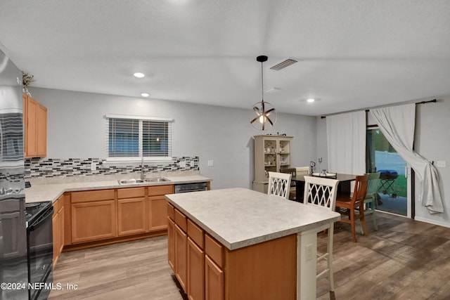 kitchen featuring tasteful backsplash, black stove, hanging light fixtures, light hardwood / wood-style floors, and a center island