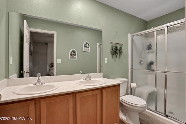 bathroom featuring toilet, a shower with door, and double sink vanity