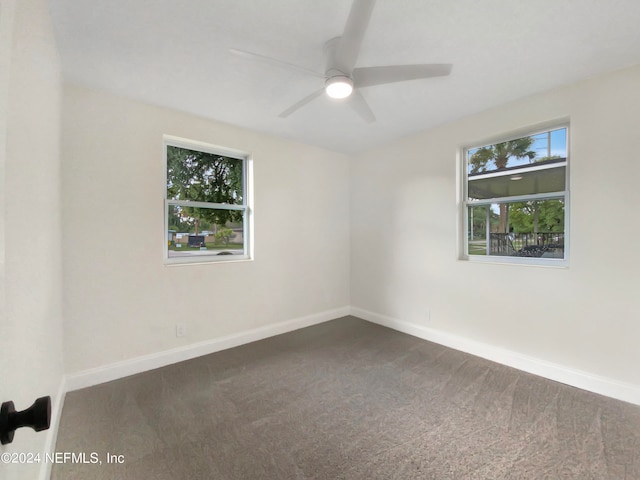 empty room with dark colored carpet, a wealth of natural light, and ceiling fan