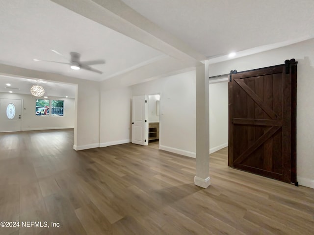 unfurnished living room featuring wood-type flooring, a barn door, and ceiling fan