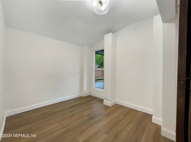 spare room featuring wood-type flooring and vaulted ceiling