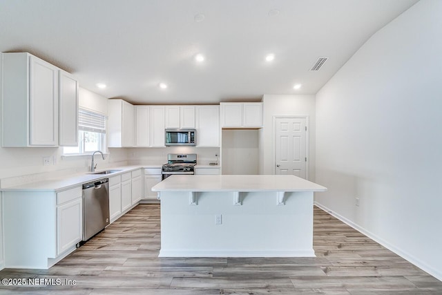 kitchen with a center island, white cabinetry, stainless steel appliances, sink, and light hardwood / wood-style flooring