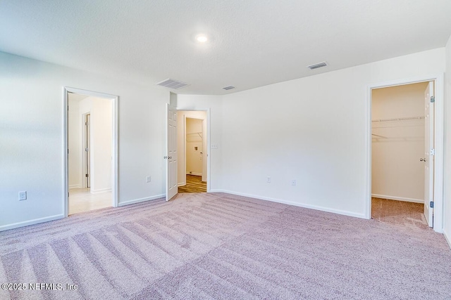 unfurnished bedroom featuring a spacious closet, a closet, and light carpet