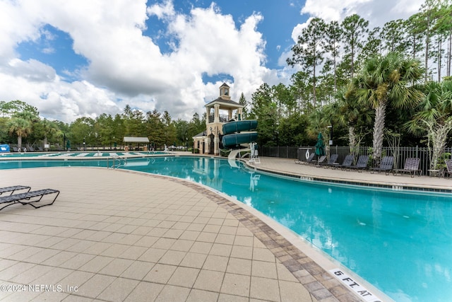 pool with a patio, a water slide, and fence