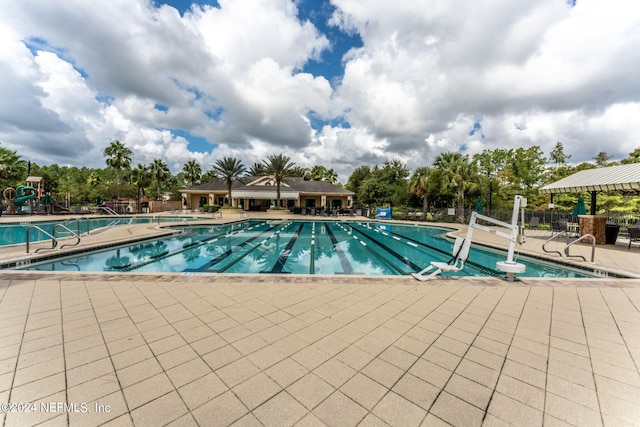 community pool with a patio area, fence, and playground community