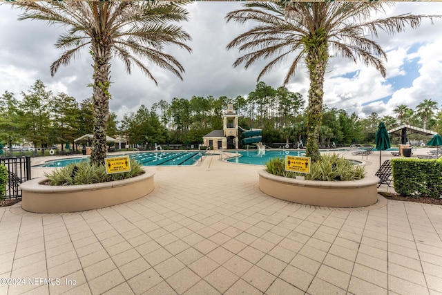 community pool featuring a water slide, a patio area, and fence