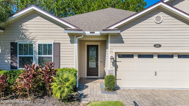 view of front of home with an attached garage, decorative driveway, and roof with shingles