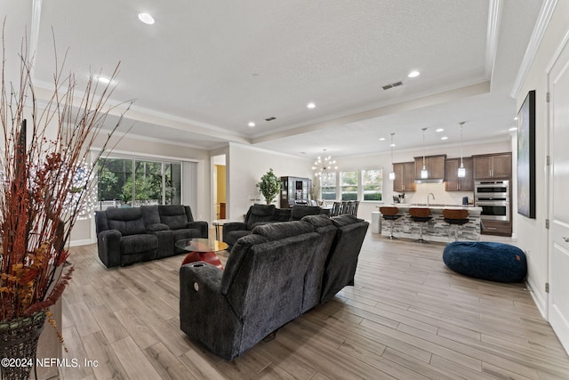 living room with light wood-type flooring, visible vents, a chandelier, and crown molding