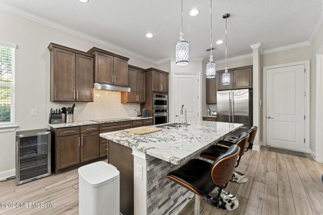 kitchen featuring a center island with sink, beverage cooler, tasteful backsplash, crown molding, and sink