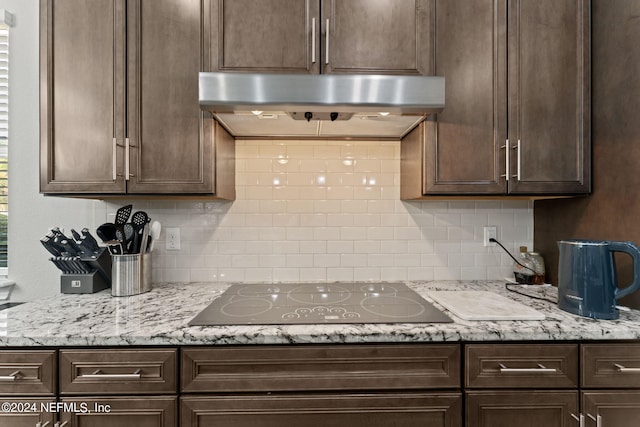 kitchen featuring dark brown cabinets, decorative backsplash, black electric cooktop, and under cabinet range hood