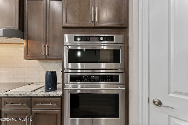 kitchen with stainless steel double oven, light stone countertops, decorative backsplash, and dark brown cabinetry