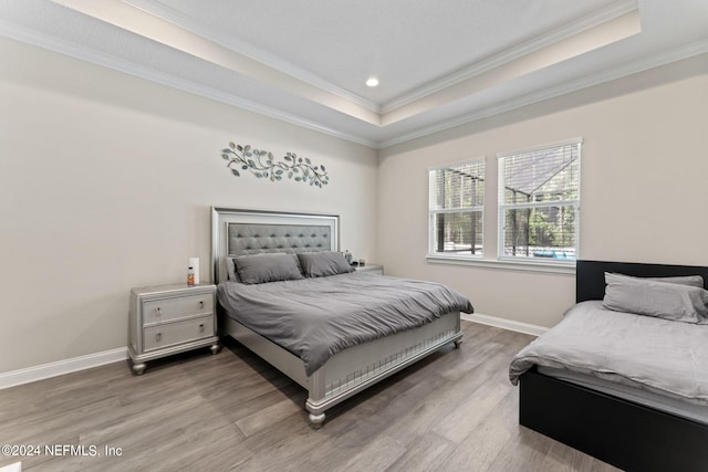 bedroom with ornamental molding, wood-type flooring, and a tray ceiling