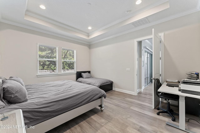 bedroom featuring light wood-type flooring, visible vents, a tray ceiling, and crown molding