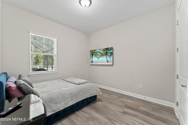 bedroom with a textured ceiling, wood finished floors, and baseboards