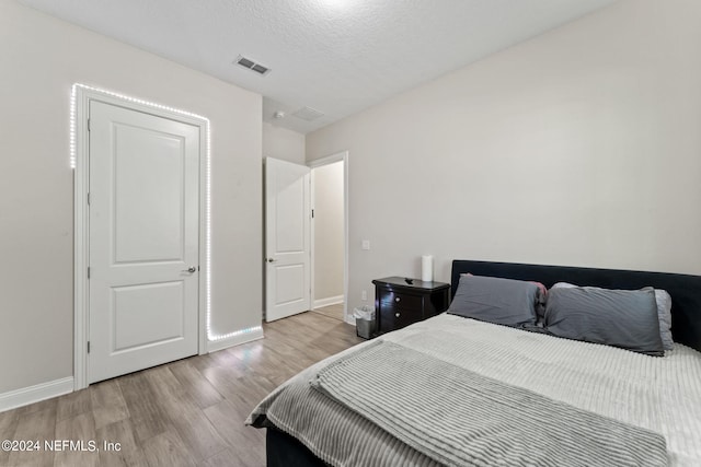 bedroom with baseboards, a textured ceiling, visible vents, and wood finished floors