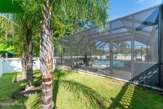 view of swimming pool with glass enclosure, a patio, a fenced backyard, a lawn, and a fenced in pool